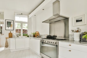 5 Ways to Clean Stainless Steel with Ingredients You Already Have at Home image showing a stainless steel range hood, backsplash, and oven in a clean white kitchen
