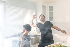 man in smoky kitchen with son while fire alarm is beeping
