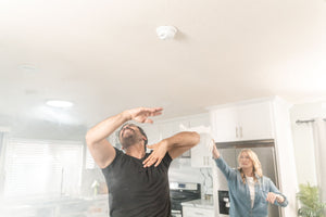 How Your Range Hood Can Save the Day When Something Burns in the Oven: two people in a smoky kitchen waving air at the smoke alarm