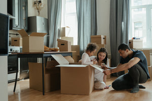 Moving? Here’s How to Ensure Your Range Hood Makes It to Your New Kitchen Intact: image showing family sitting on the floor packing boxes in the kitchen preparing for a home move